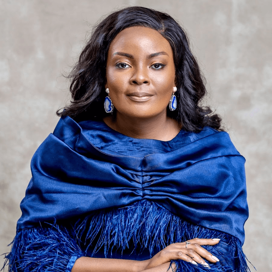 Dr. Love Ogah, smiling warmly in a royal-blue shawl against a soft neutral backdrop.